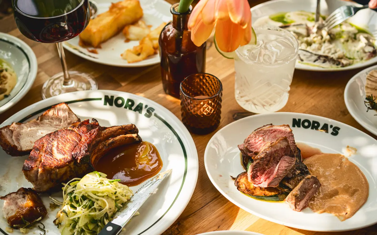 Charcoal-grilled steaks and plates spread across a table at NORA'S